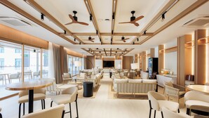 Un espacioso vestíbulo de hotel con techos altos, ventiladores de techo y una zona de estar central con sofás y sillones.