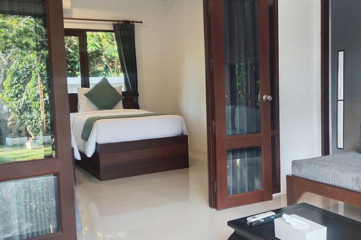 A bedroom with a bed, a sofa, and a small table. There are glass doors leading to a balcony.