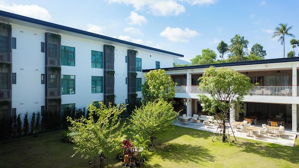 Un edificio moderno con varios balcones, un patio con vegetación y zona de estar al aire libre.