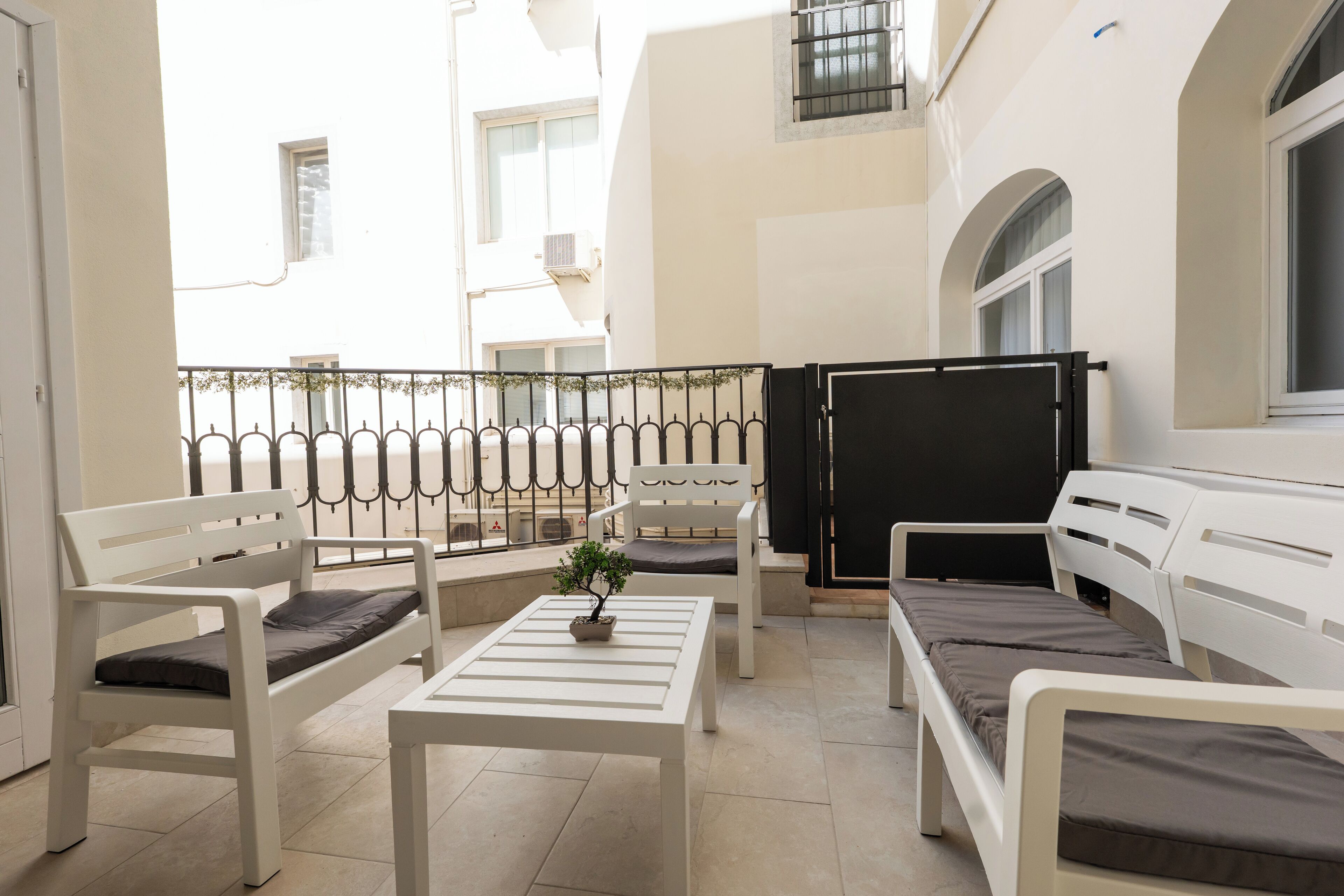 Ein Balkon mit weißer Möbel, darunter Bänke und ein Tisch, sowie ein Blumentopf.