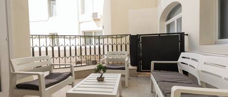 A balcony with white furniture, including benches and a table, and a potted plant.