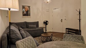 A living room with a sofa, a round table, a fan, a lamp, and a chandelier.