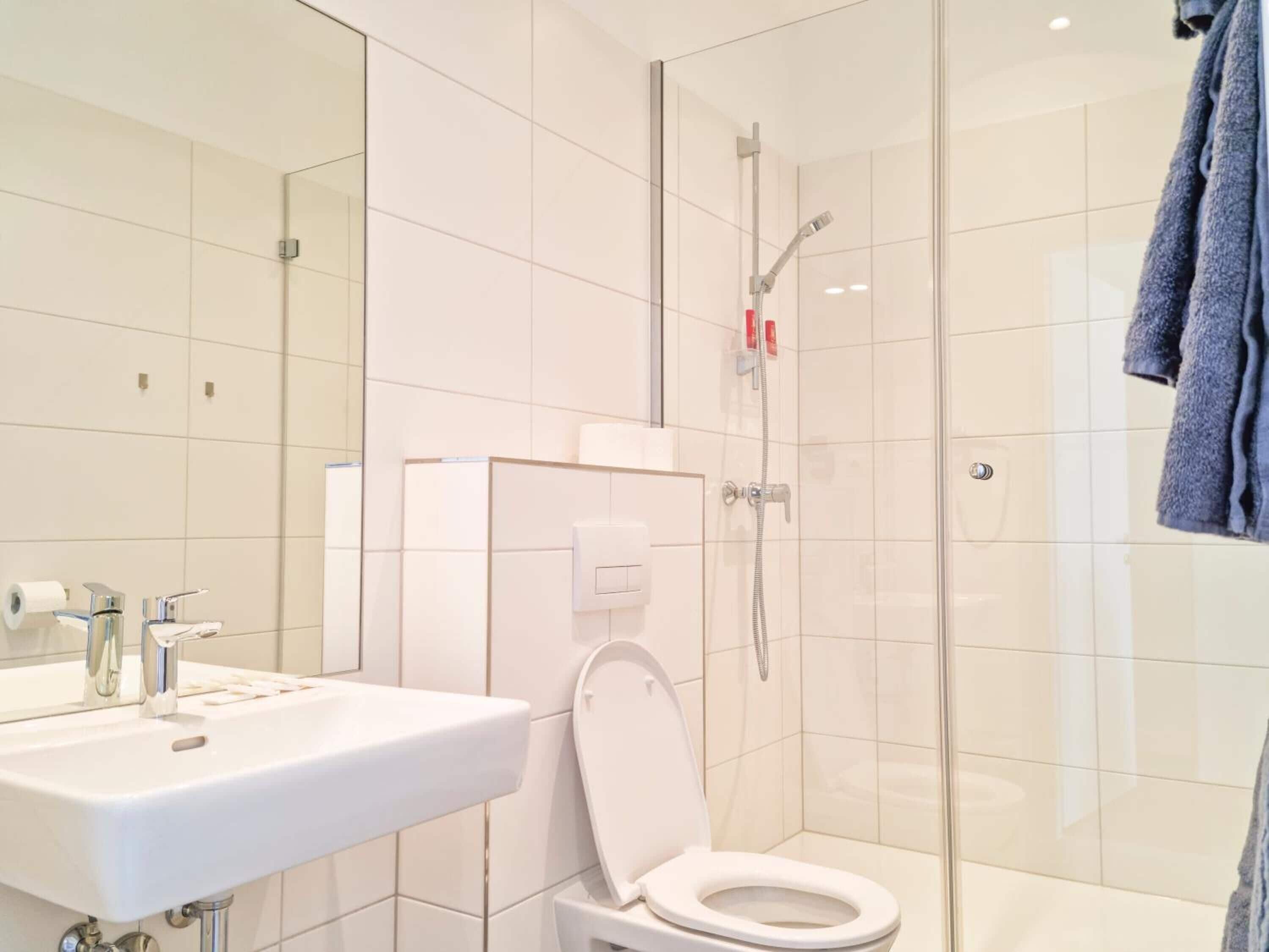 Un baño moderno con lavamanos blanco, inodoro y cabina de ducha con paredes de vidrio.