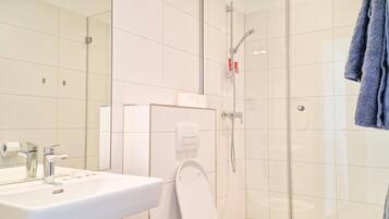 Un baño moderno con lavamanos blanco, inodoro y cabina de ducha con paredes de vidrio.