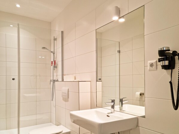 Un bagno moderno con box doccia in vetro, lavabo bianco con specchio e asciugacapelli montato a parete.