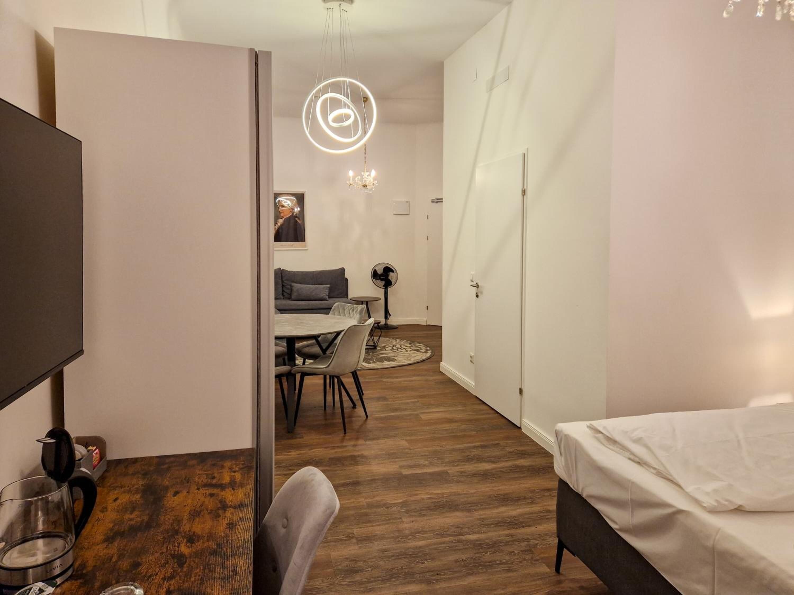 Een moderne kamer met houten vloer, een bed, een eettafel met stoelen, een televisie en een kroonluchter.