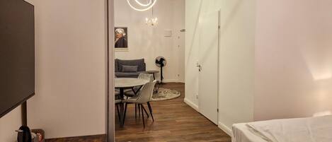 Een moderne kamer met houten vloer, een bed, een eettafel met stoelen, een televisie en een kroonluchter.