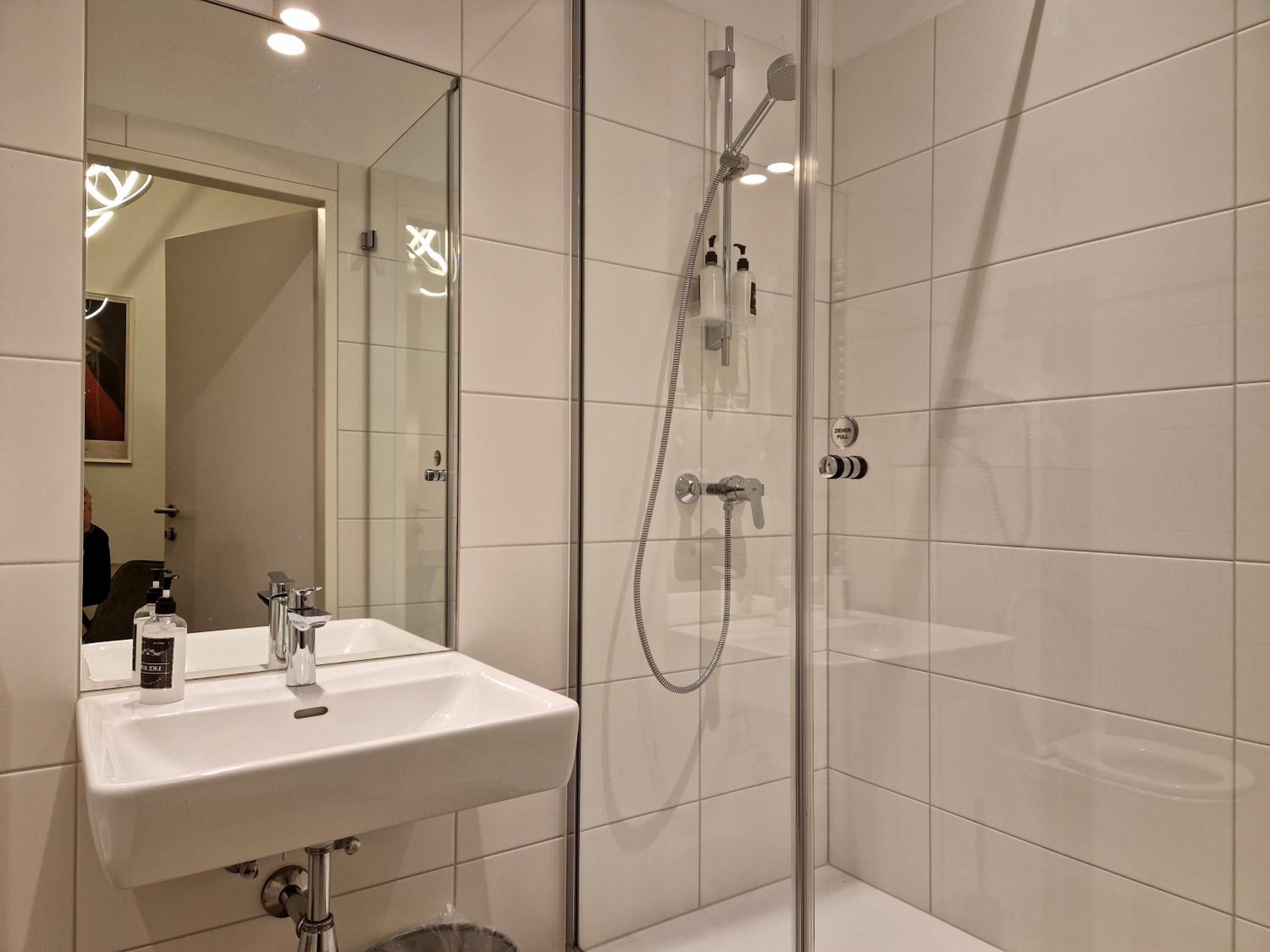 Une salle de bain moderne avec une douche à parois de verre, un lavabo blanc avec un miroir et des toilettes apparentes.