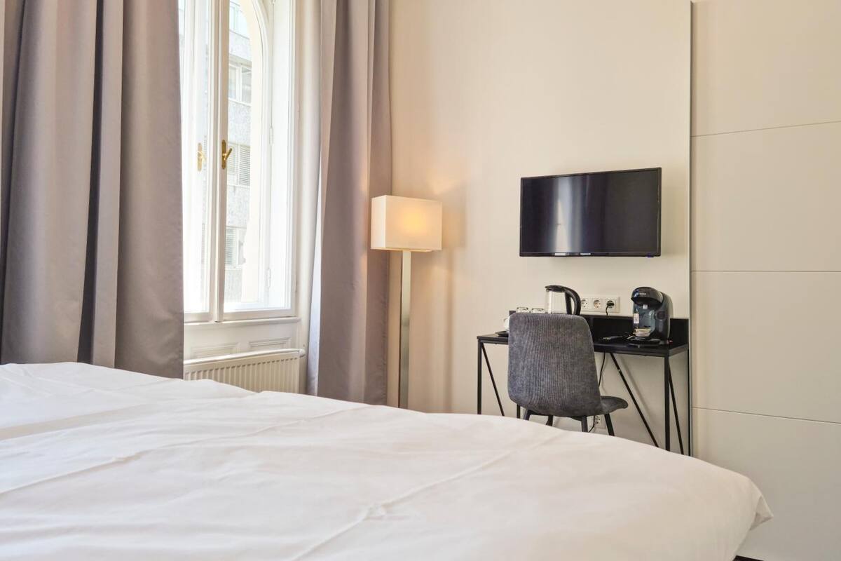 Ein Hotelzimmer mit einem Bett, einem Schreibtisch mit Stuhl, einem Fernseher und einem Fenster mit Vorhängen.