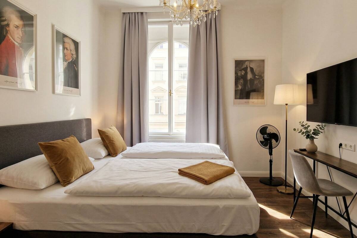 Ein Hotelzimmer mit einem großen Bett, einem Schreibtisch mit Stuhl, einem Fernseher und einem Fenster mit Vorhängen.