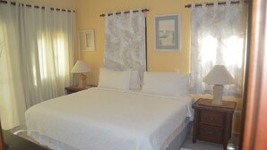 A neatly made bed with white linens, two bedside tables with lamps, and a framed picture on the wall. - Beach apartment stanza mare (Punta Cana)