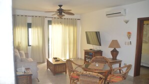 A living room with a sofa, coffee table, dining table with chairs, a television, and a ceiling fan. - Beach apartment stanza mare (Punta Cana)