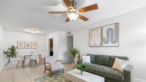 Ein modernes Wohnzimmer mit Deckenventilator, einem grünen Sofa, einem weißen Couchtisch und einem Essbereich mit Stühlen und einem Tisch.
