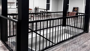 A spacious room with a high ceiling, black metal railings, and a modern kitchen area in the background. - BRAND NEW, SPACIOUS, FUN - The Wolves Den on Fraley (Kane)