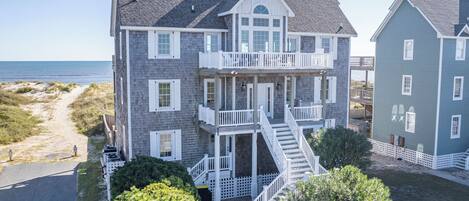 A two-story house with a balcony, a staircase, and a view of the beach.
