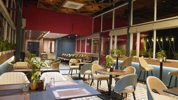 Un restaurante con una decoración moderna, que ofrece una variedad de opciones de asientos como cabinas y mesas, con plantas en macetas y un suelo con diseño.