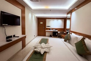 Habitación de hotel con cama, escritorio, silla, televisión y una escultura de toallas.