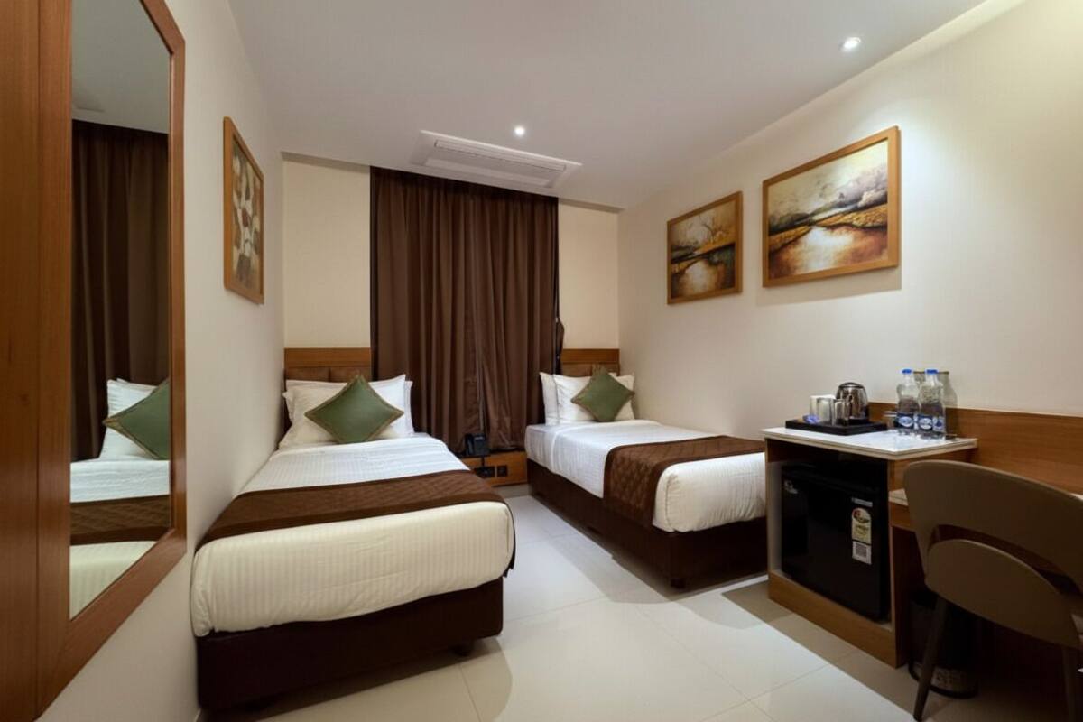 A hotel room with two beds, a desk, a chair, a coffee maker, and a small refrigerator.