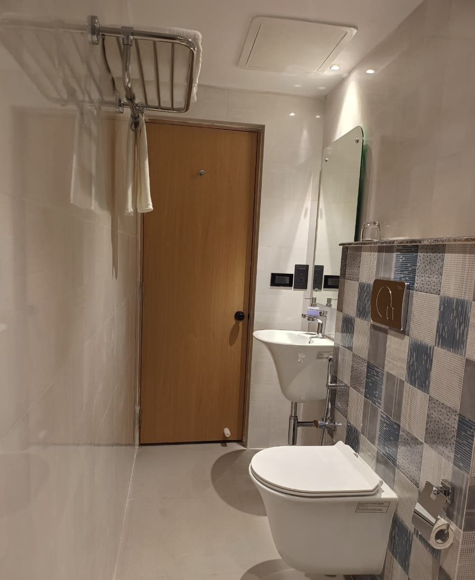 A modern bathroom with a wooden door, a white toilet, a sink with a mirror above it, and a shower area with a towel rack.