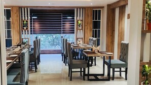 A restaurant with multiple tables and chairs, a wooden interior, and large windows. - Hotel Green View (Berhampore)