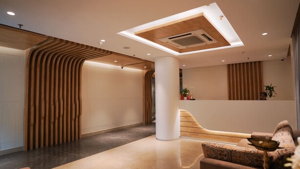 A modern lobby with a curved wooden wall, a central column, and a seating area with patterned cushions. - Hotel Green View (Berhampore)