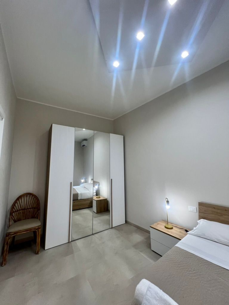 A modern bedroom with a bed, a nightstand, a chair, and a wardrobe.
