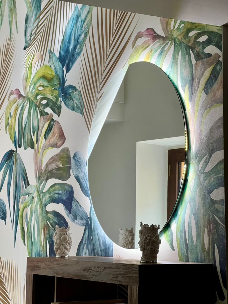 A bathroom with a large mirror, a wooden vanity, and a floral wallpaper design.