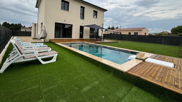 Ein modernes Haus mit Swimmingpool, einer Terrasse mit Liegestühlen und einem gepflegten Rasen.