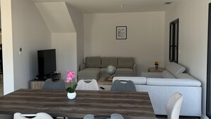 Ein modernes Wohnzimmer mit einem Holzesstisch, grau gepolsterten Sesseln, einem grauen Sofa und einem Flachbildfernseher.