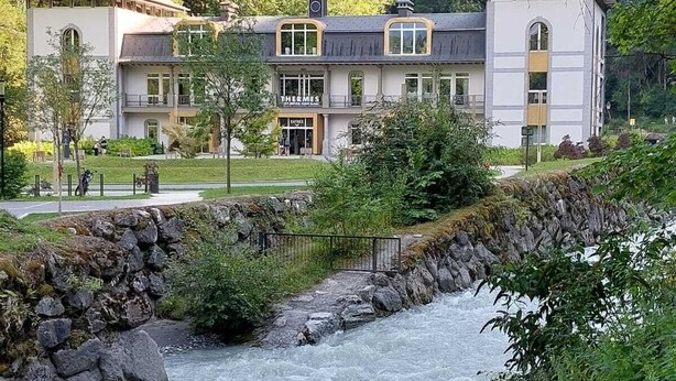 Een hotel met een modern design, met een centrale ingang, meerdere ramen en uitzicht op een rivier.