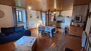 Een gezellige woonkamer met een bank, een eettafel met stoelen en een keuken met fornuis en kastjes.