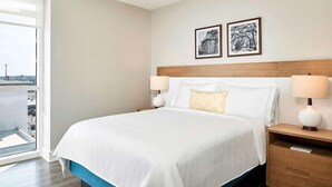 A hotel room with a large bed, two bedside lamps, a nightstand, and a view of the city through a large window. - Ocean Enclave July 4th weekend. Beachfront hotel. Partial Ocean View 1 bedroom. (Myrtle Beach)