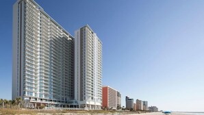 A high-rise hotel with multiple floors and balconies, located near a beach. - Ocean Enclave July 4th weekend. Beachfront hotel. Partial Ocean View 1 bedroom. (Myrtle Beach)