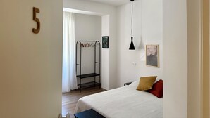 A bedroom with a bed, a hanging lamp, a wall-mounted shelf, and a door with a number. - B&B Loggia Garbatella (Rome)