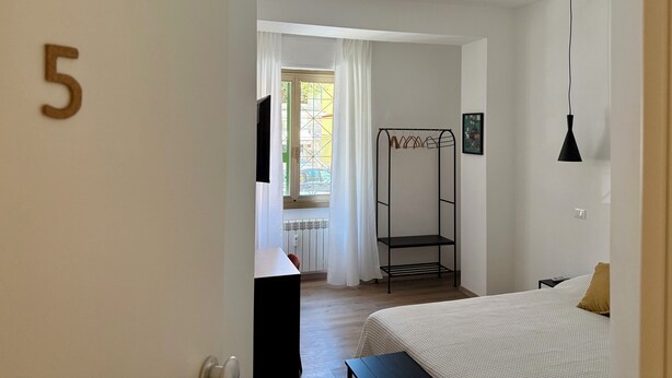 A bedroom with a bed, a hanging light fixture, a coat rack, and a door with the number 5. - B&B Loggia Garbatella (Rome)