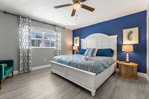 A bedroom with a white bed, blue bedding, a teal armchair, a ceiling fan, and a window with patterned curtains. - 5-Bedroom Sarasota Retreat with Heated Pool mins to Siesta Beach/NO CLEANING FEE (Sarasota)