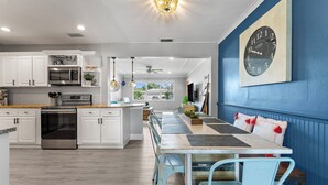 Een moderne keuken met witte kasten, roestvrijstalen apparatuur en een eethoek met een blauwe wand en een klok.