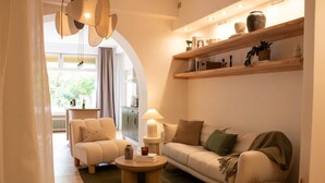 A cozy living room with a sofa, a coffee table, and a lamp. There is a bookshelf with decorative items and a window with curtains. - Documenta - With a terrace and a view of the countryside (Kassel)