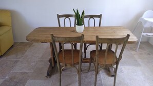 A wooden dining table with four chairs, a potted plant, and a yellow sofa in a room with tiled flooring. - Large, renovated country house. Children and pets welcome! (Chaumard)