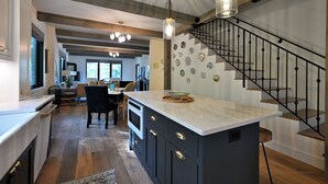 Una cocina moderna con una isla central, vigas de madera y una escalera con barandilla negra.