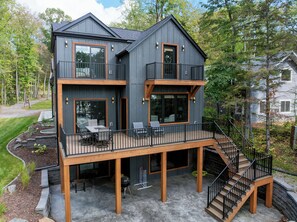 Una casa de dos pisos con un balcón, mobiliario exterior y una escalera que conduce al nivel superior.