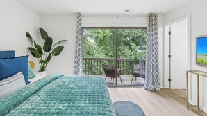 Un dormitorio con cama, planta en maceta, balcón con sillas y televisor.
