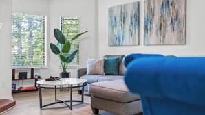 Una sala de estar moderna con un sofá gris, una mesa de centro redonda y una gran planta en maceta.