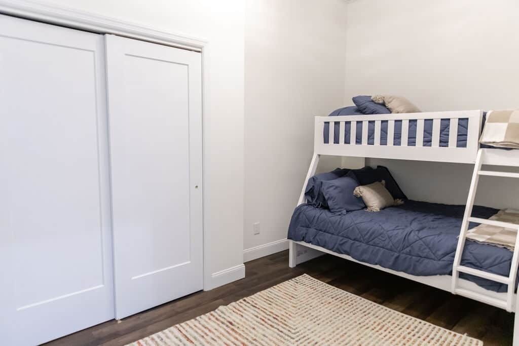 A bedroom with a bunk bed, a wardrobe, and a patterned rug.