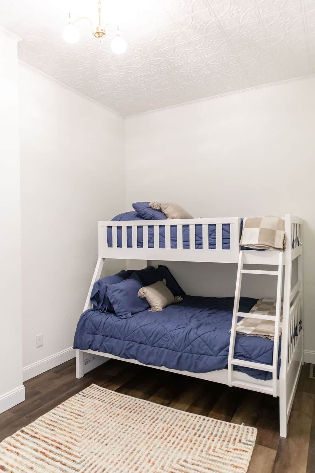 A bunk bed with a blue mattress and pillows, a white headboard, and a wooden floor.
