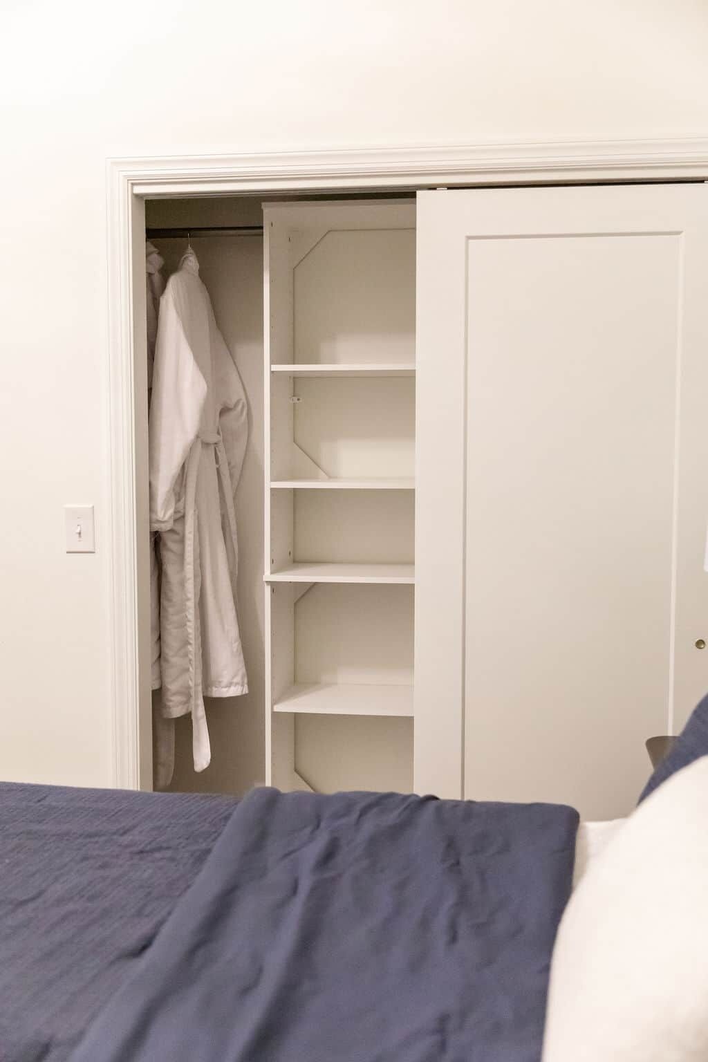A bedroom with a bed, a wardrobe with hanging clothes, and a door.