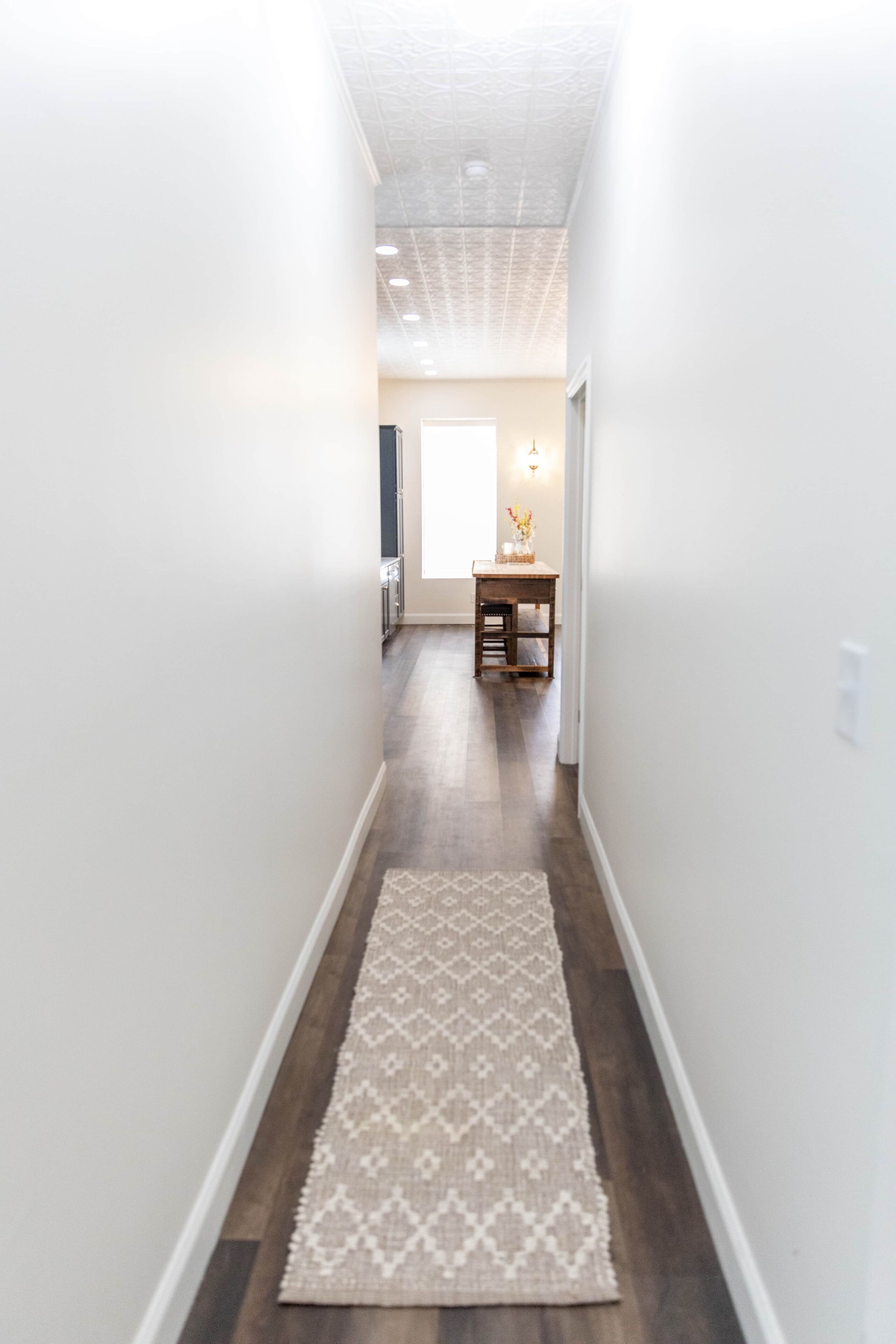 Un corridoio con tappeto a motivi, pavimento in legno e soffitto con illuminazione incassata.