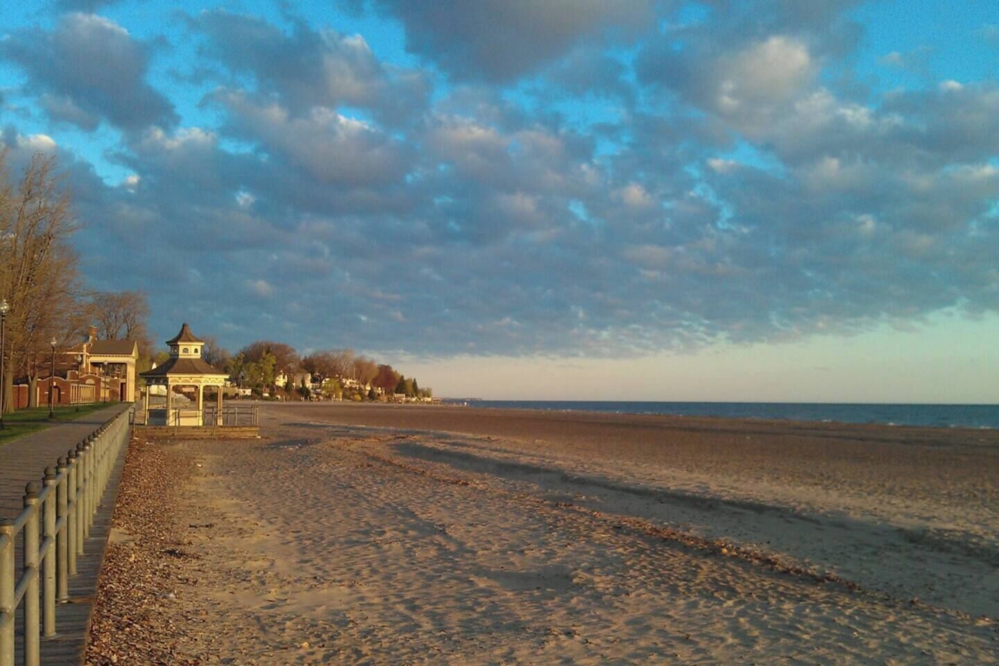 A beach with a gazebo, a fence, and buildings in the background.