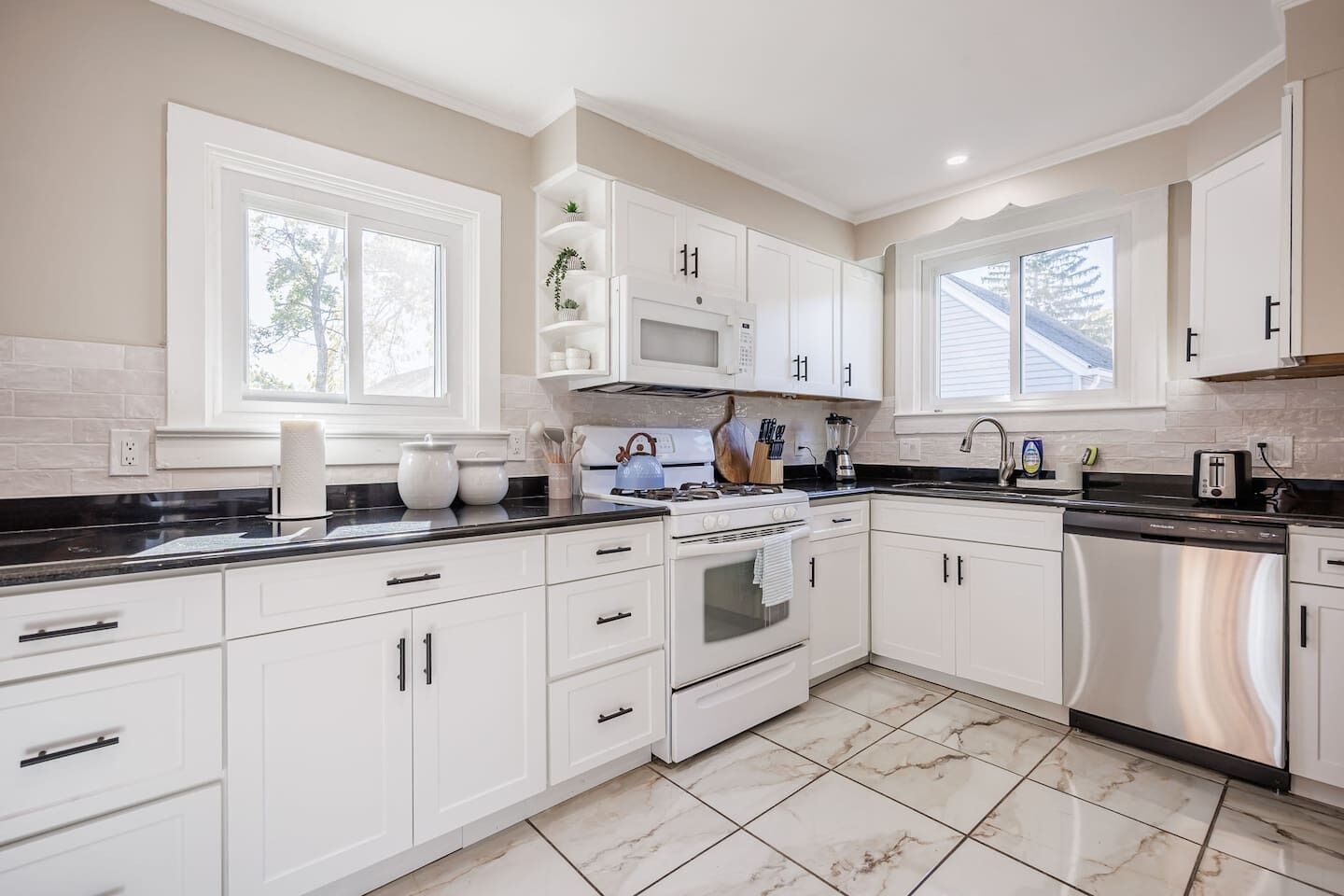 A modern kitchen with white cabinetry, a black countertop, and a stainless steel dishwasher.