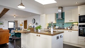 Una cocina moderna con armarios blancos, una isla central y un área de comedor con un sofá de cuero marrón.